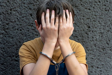 Person with hands covering face, wearing handcuffs, Legal Consequences.
